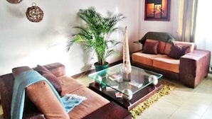 Un salon avec un plafond en bois, un ensemble de canapés, une table basse, une plante en pot et un tableau accroché au mur.