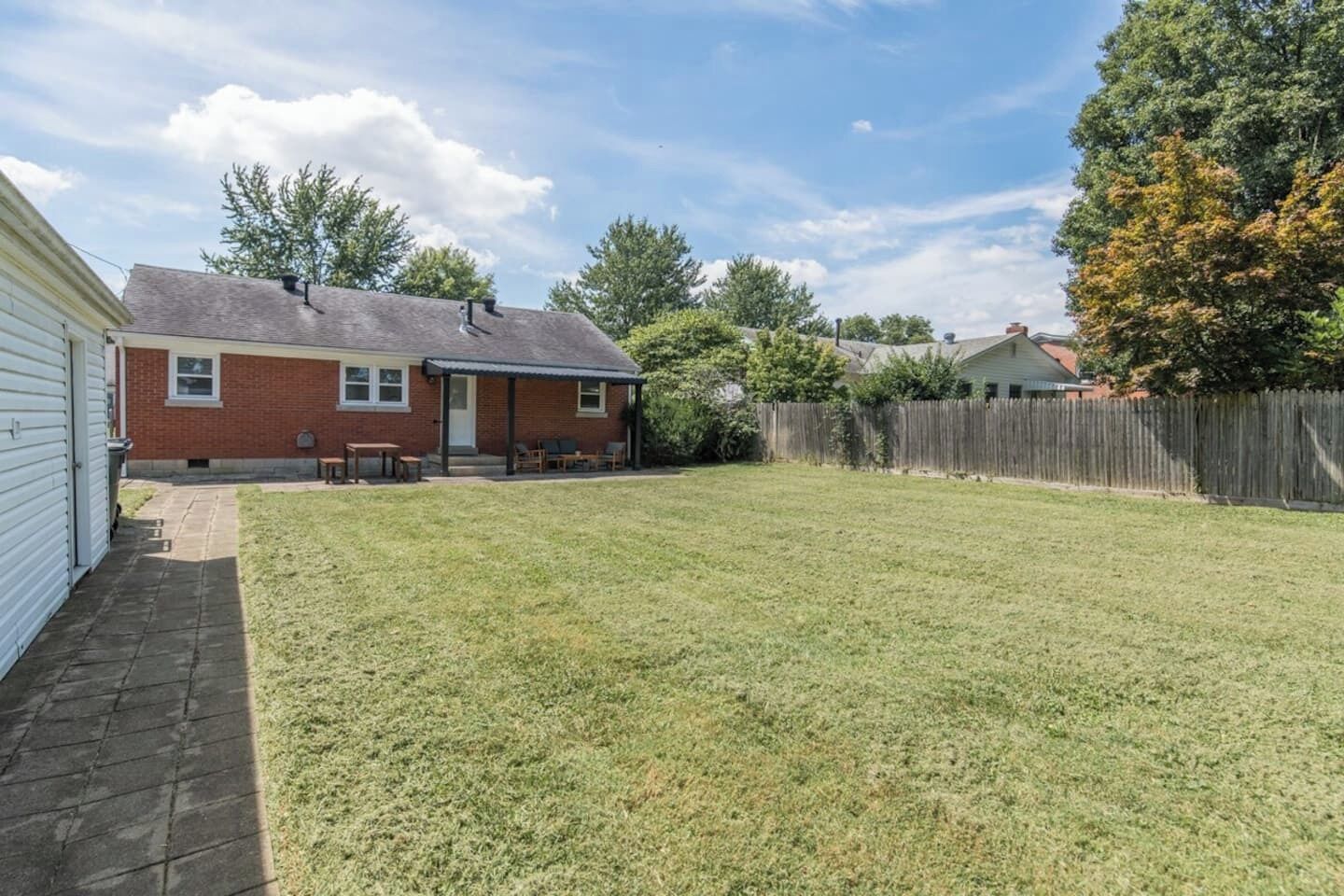 A residential backyard with a brick house, a wooden deck, and a fenced area.