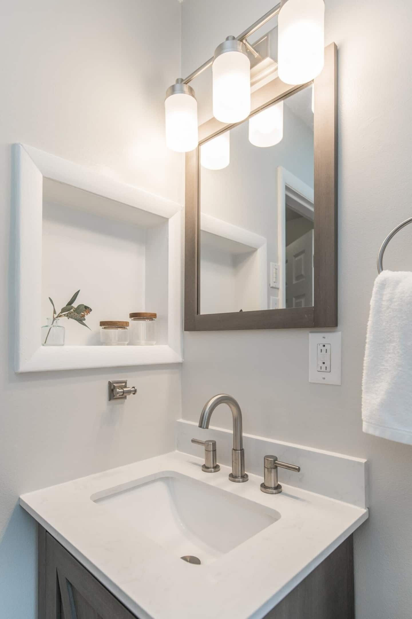 A modern bathroom with a white sink, a large mirror, and a light fixture above the mirror.