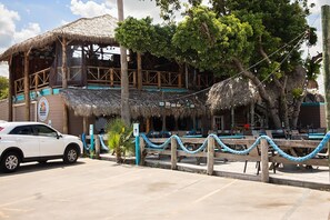 Un bâtiment en bois avec un toit de chaume, une barrière en corde bleue et une voiture blanche garée devant.