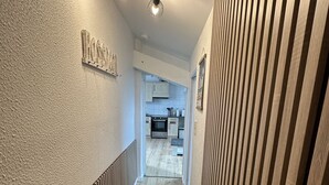 Un couloir avec un plancher en bois, un luminaire au plafond et une cuisine visible au fond.