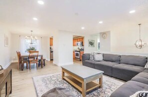 A modern living room with a grey sofa, a wooden coffee table, and a dining area with wooden chairs and a table.