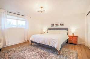 A bedroom with a bed, nightstands, a rug, and a window with curtains.