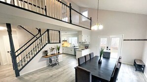 A spacious living area with a dining table, a staircase, and a kitchen in the background.