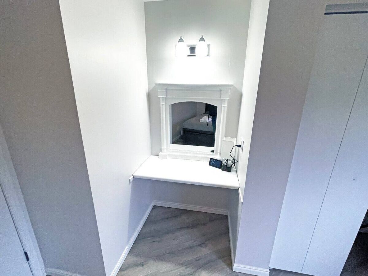 A narrow hallway with a white wall, a small window, and a white bench.