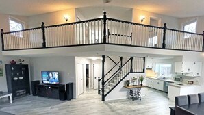 A spacious living area with a high ceiling, a staircase leading to an upper level, a television, and a kitchen area.