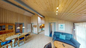 A spacious room with wooden walls and ceiling, a dining area with a table and chairs, a sofa, and a kitchen area with cabinets and a stove. - 2 bedroom stunning home in Rechlin (Rechlin)