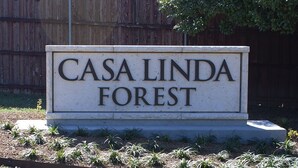 A sign for "Casa Linda Forest" with a wooden fence and greenery in the background.