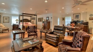 A spacious living room with a large bed, leather armchairs, a dining area, and a kitchen.
