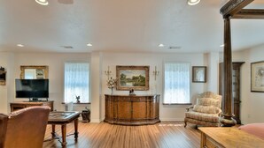 A spacious living room with hardwood flooring, a large wooden cabinet, a television, and a comfortable armchair.