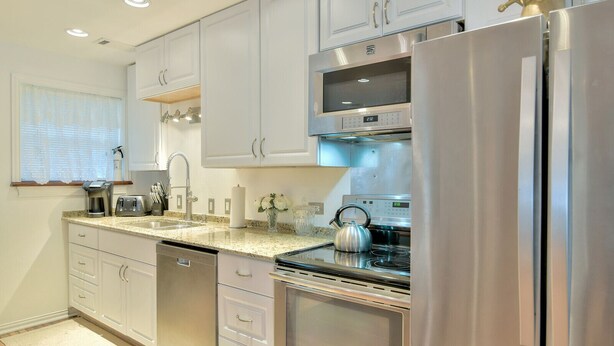 A modern kitchen with stainless steel appliances, white cabinetry, and a granite countertop.