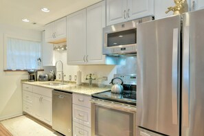 A modern kitchen with stainless steel appliances, white cabinetry, and a granite countertop.