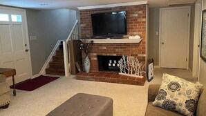 Ein Wohnzimmer mit Kamin, Fernseher und einer Treppe, die in eine andere Ebene führt.