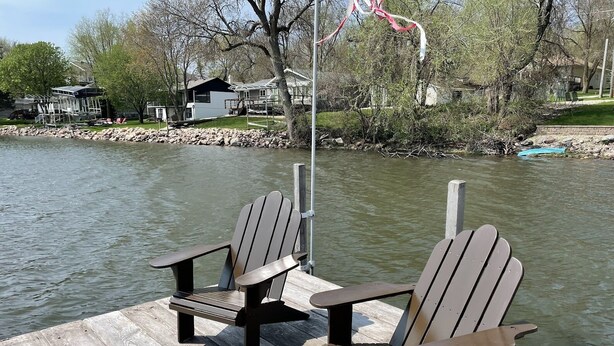 Zwei Adirondack-Stühle an einem hölzernen Steg an einem ruhigen Fluss.