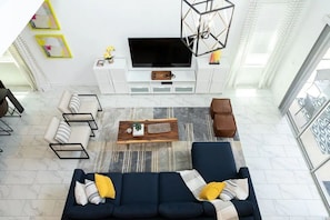 Uma sala de estar moderna com um sofá azul-escuro, uma mesa de centro de madeira e uma televisão de tela plana sobre um móvel branco.