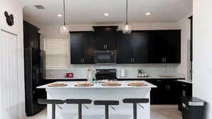 A modern kitchen with dark cabinets, a white island with stools, and pendant lighting.