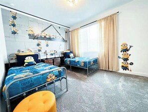 Quarto infantil com duas camas, uma escrivaninha e uma cadeira.