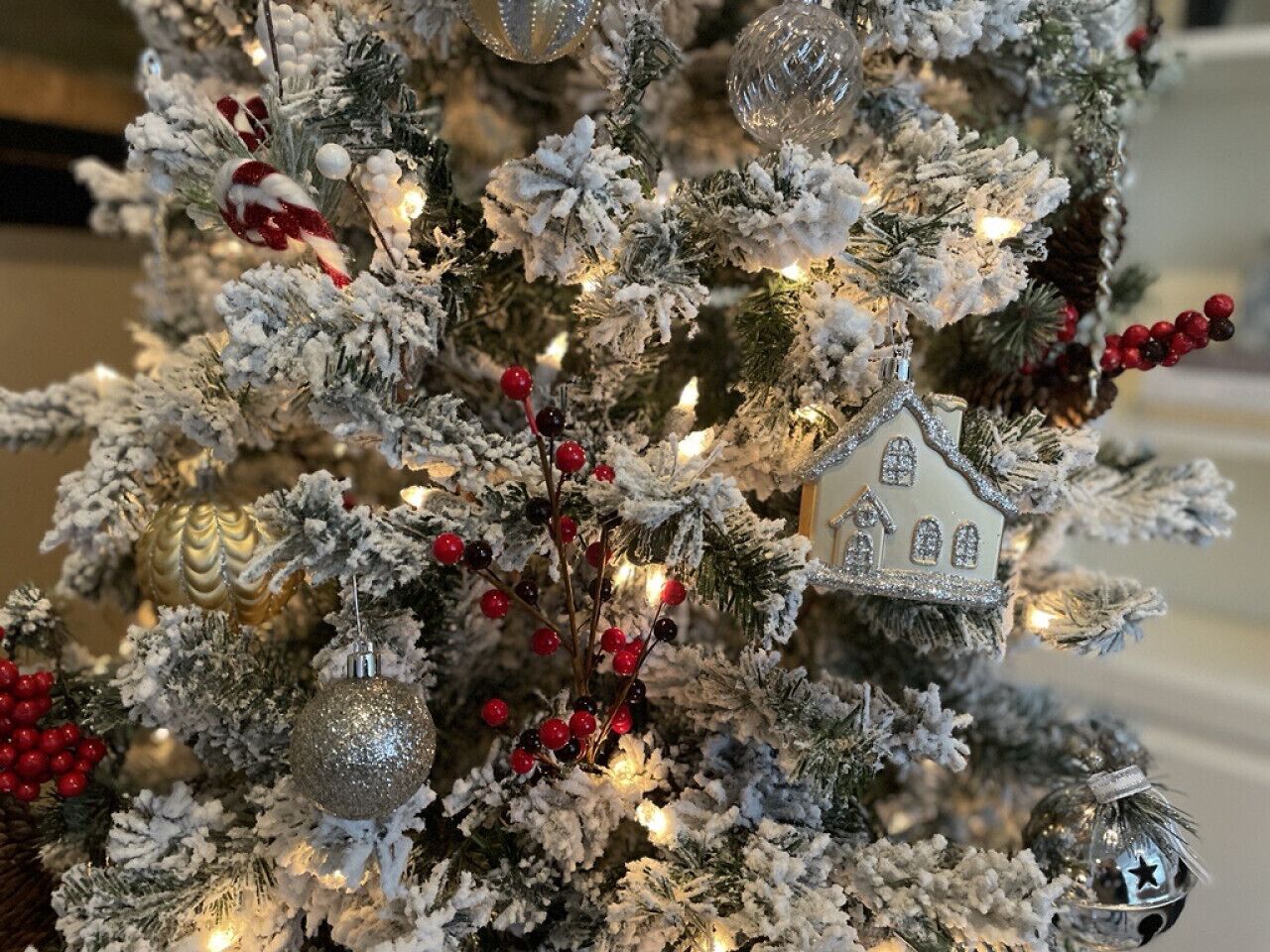 A Christmas tree with snow-like decorations, red berries, and a house ornament.