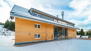 Ein modernes Holzgebäude mit großen Fenstern und einem überdachten Eingang, umgeben von Schnee.