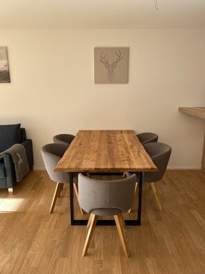 A dining area with a wooden table and grey upholstered chairs, a grey sofa with a blanket, and a wall-mounted artwork.