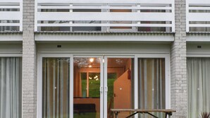 Un edificio moderno con un balcone, ampie porte scorrevoli in vetro e un piccolo tavolo da esterno.