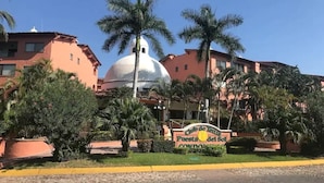 A building with a dome and palm trees, a sign reading "Ciudad de la Salud", and a paved street in front. - CONDO PSOL BY TRVL2HM (Puerto Vallarta)