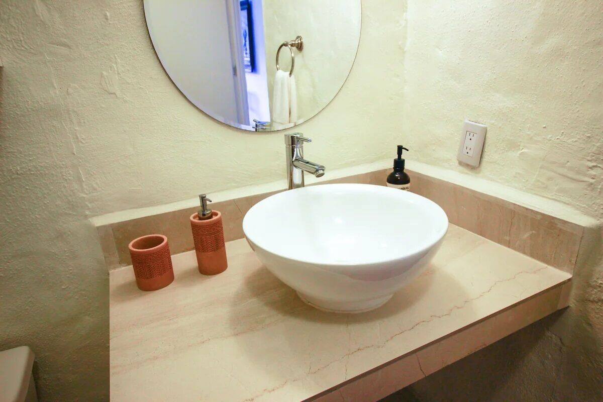 A bathroom with a white sink, a round mirror, and two red candle holders.