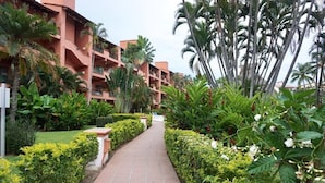 A pathway leading to a building with multiple balconies, surrounded by lush greenery and palm trees. - CONDO PSOL BY TRVL2HM (Puerto Vallarta)