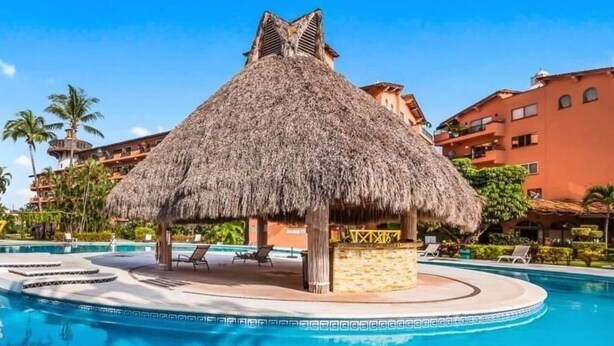 A pool area with a thatched-roof structure, lounge chairs, and a clear blue pool. - CONDO PSOL BY TRVL2HM (Puerto Vallarta)
