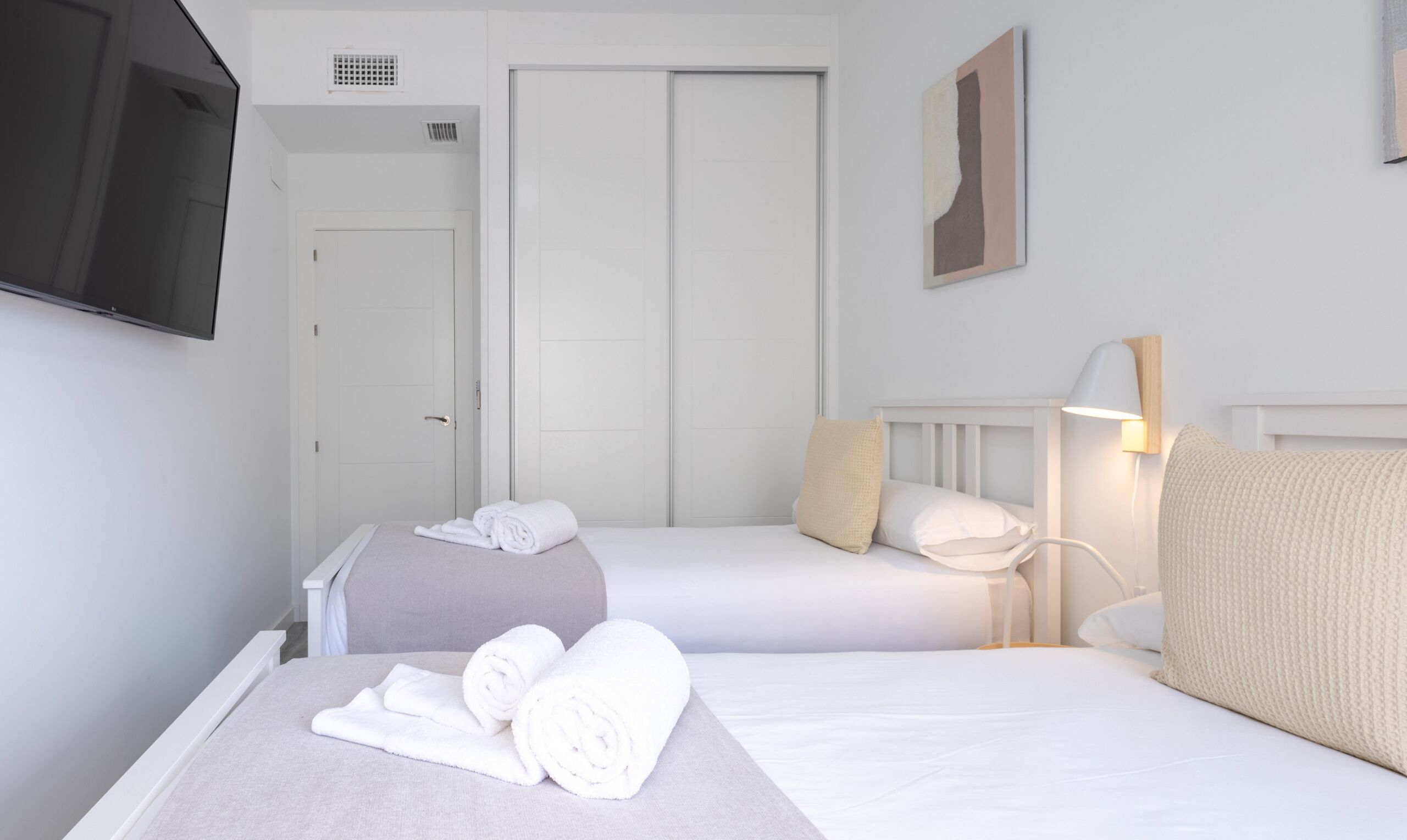 A hotel room with two beds, a TV, a wardrobe, and a bedside lamp.