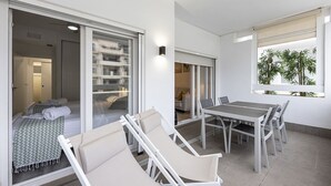 A modern balcony with a dining table and chairs, a sofa, and a view of a building and plants. - Ref. 377638 (Motril)