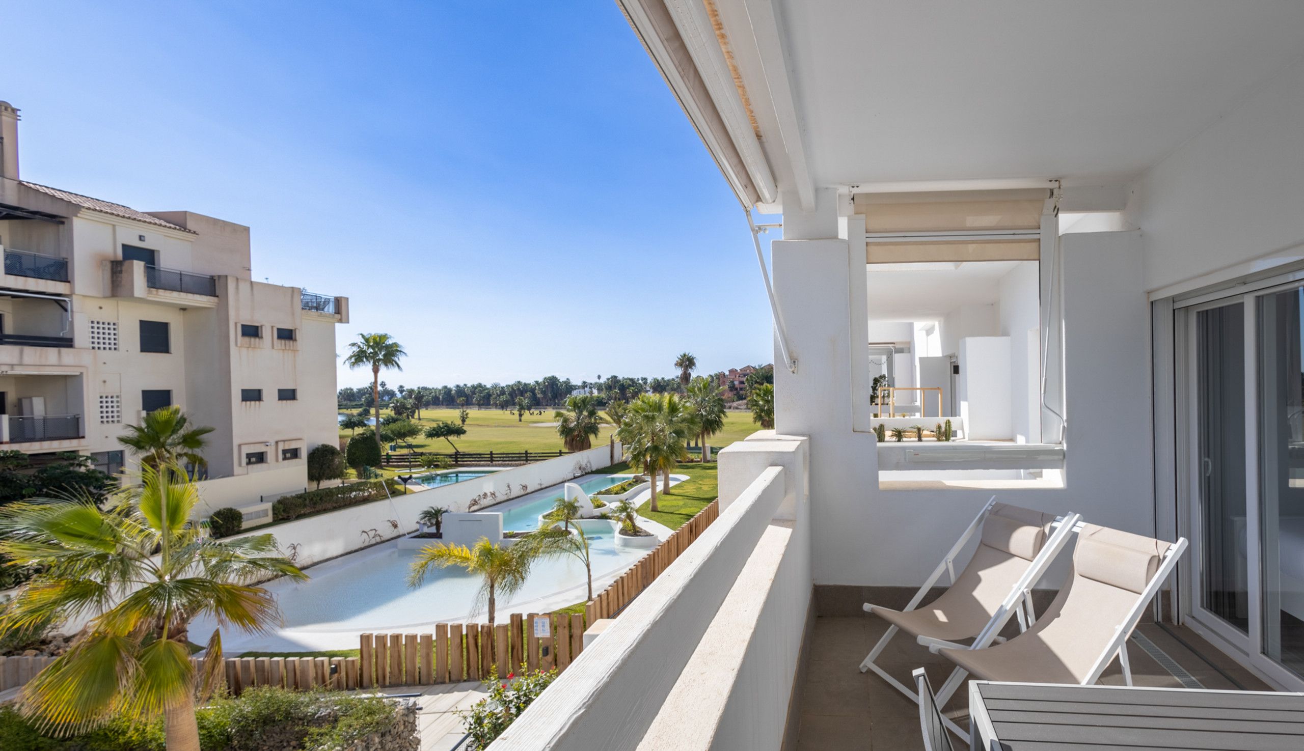 Un balcon avec vue sur la piscine, des chaises longues et un ciel dégagé.