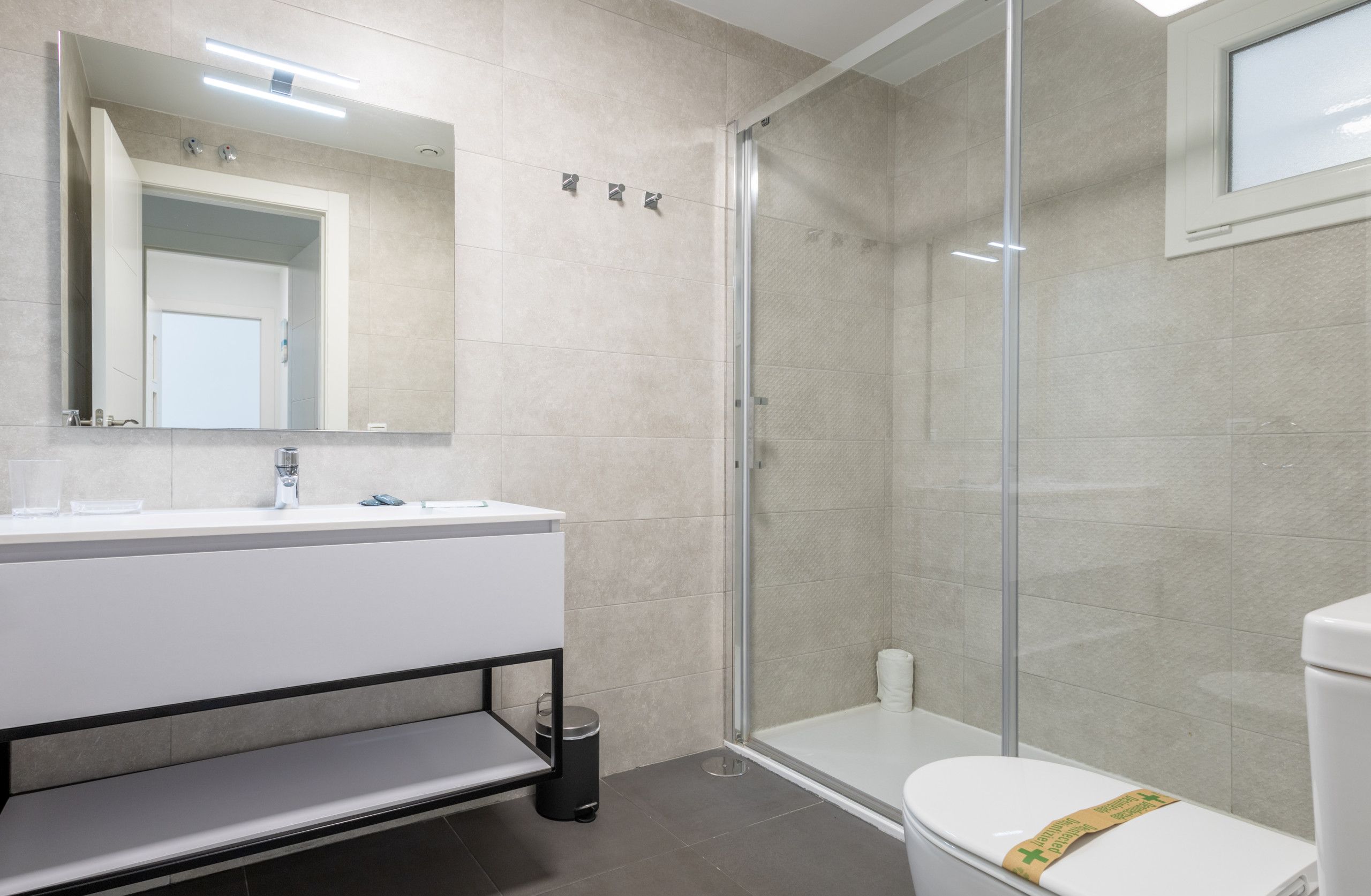 Een moderne badkamer met een douchecabine van glas, een wit wastafelmeubel met spiegel en een toilet.