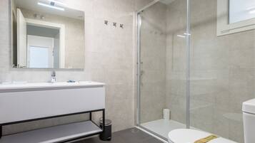 Een moderne badkamer met een douchecabine van glas, een wit wastafelmeubel met spiegel en een toilet.