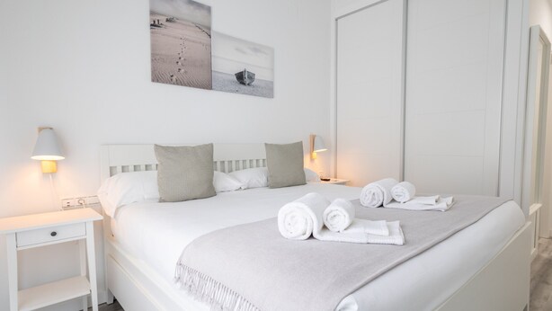 A neatly made bed with rolled towels, a bedside table with a lamp, and a wall-mounted artwork depicting a boat on a beach. - Ref. 377638 (Motril)