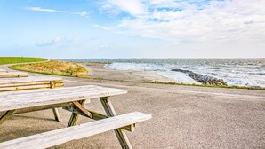 Et picnicbord langs en asfalteret sti med udsigt over en strand, hvor bølgerne skummer.