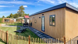 En moderne træbygning med en glasdør, en terrasse med bord og stole, og en indhegnet gård.