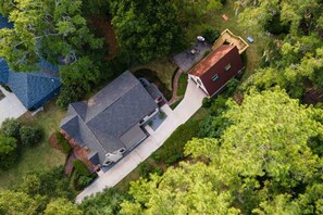 An aerial view of a residential area with two houses, one with a red roof and another with a blue roof, surrounded by dense greenery.
