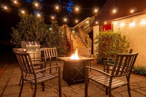 An outdoor patio with a grill, a fire pit, and wooden chairs.