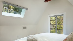 Een slaapkamer met dakraam, groot raam en een opgemaakt bed.