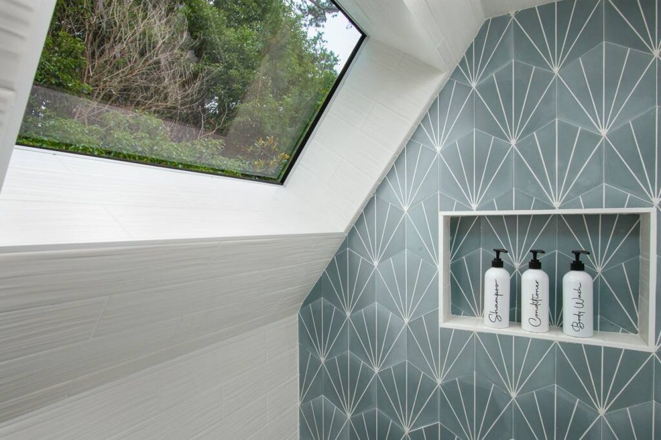 A bathroom with a skylight, geometric wall tiles, and a shelf with toiletries.