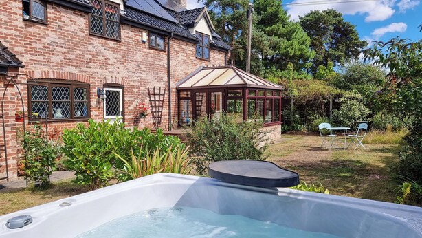 Un jacuzzi dans un jardin, avec une maison en briques et une pergola en bois.