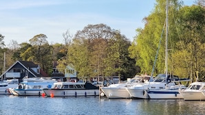 Un port de plaisance où sont amarrés plusieurs bateaux, entouré d’arbres et bordé d’un bâtiment doté d’un toit en pente.