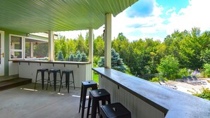 A covered outdoor area with a bar and stools, overlooking a garden with trees and a patio with lounge chairs. - 9 Bedroom Estate, Sleeps 24, Pool, Hot Tub, Movie Theater, Game Room (Newry)