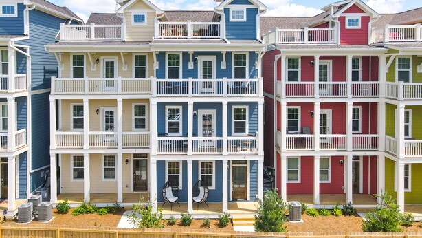 Une rangée de maisons de ville colorées à deux étages, dotées de balcons, avec une clôture en bois au premier plan et un ciel dégagé.
