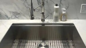 Una cocina con salpicadero de mármol, un lavamanos de acero inoxidable con grifo de manguera y dos botellas de jabón sobre la encimera.