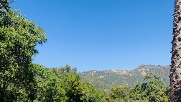 Un patio exterior con mobiliario de madera, una mesa de piedra y vistas a montañas.