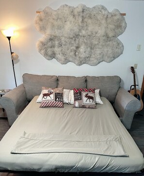 A bed with a beige cover, a grey sofa, and a wall-mounted fluffy decoration.