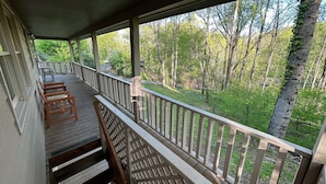 A covered porch with wooden railings and a view of a forested area.