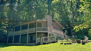 A two-story house with a balcony, surrounded by a lush green landscape.